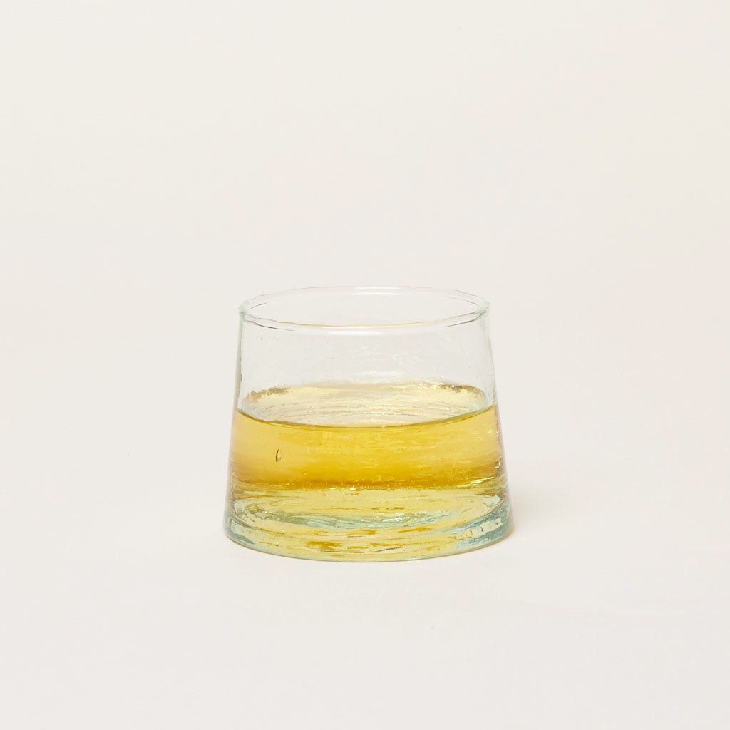 A short cylindrical drinking glass that tapers toward the rim contains yellow liquid