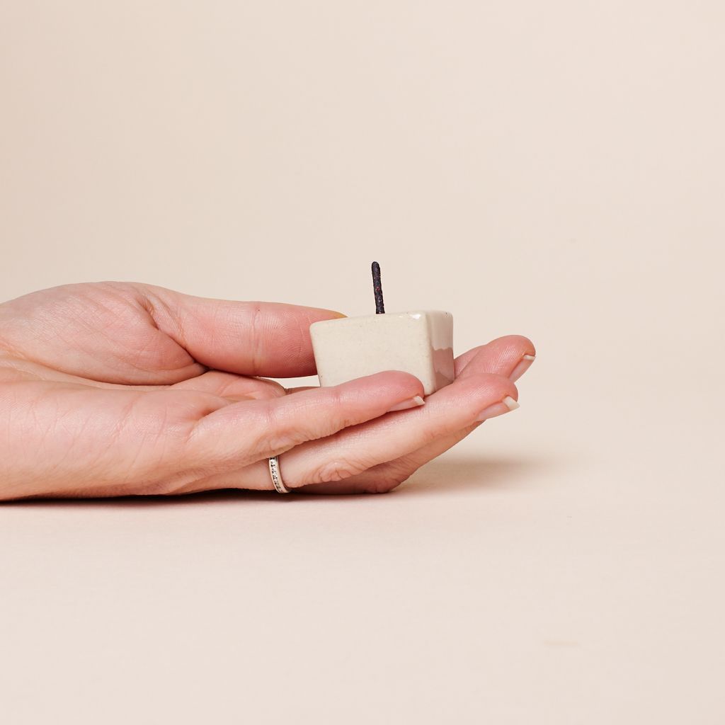A hand with upward-facing palm hold a ceramic candle holder that is square and beige