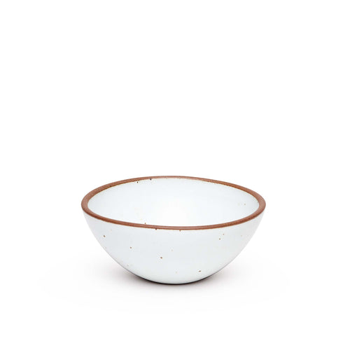 A medium rounded ceramic bowl in a cool white color featuring iron speckles and an unglazed rim