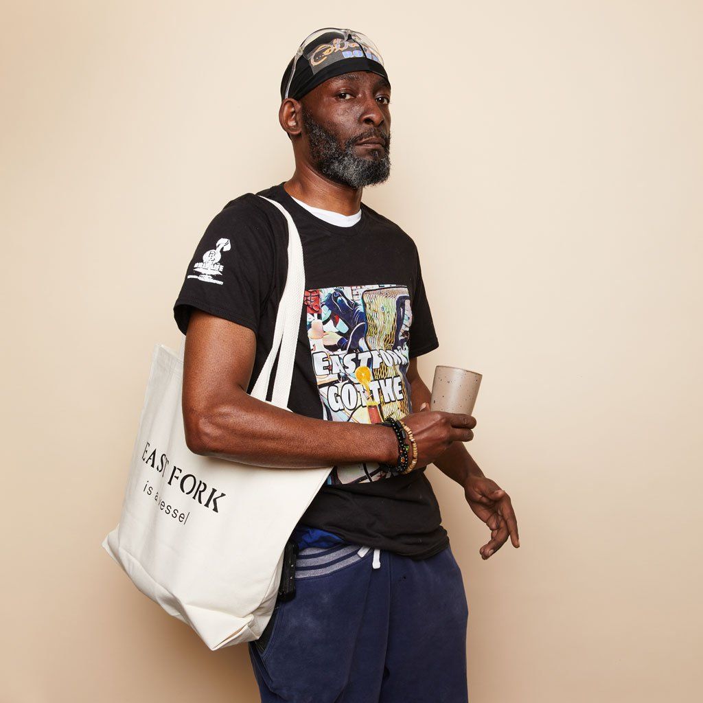 A person in a Drip Life tee holds a Juice Cup and wears an East Fork tote bag on shoulder.