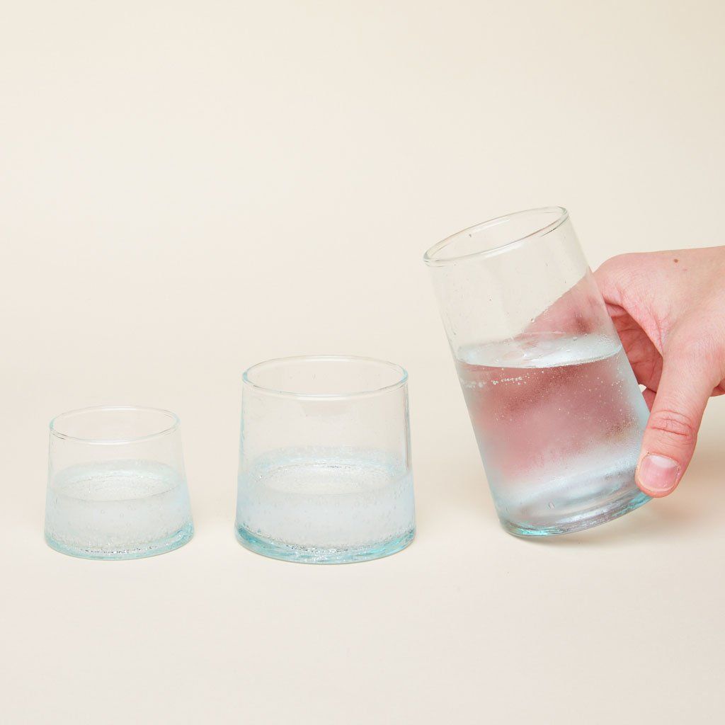 Hand holds tall drinking glass. Also shown, glass in small and medium sizes.